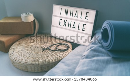 Yoga breathing INHALE EXHALE sign at fitness class on lightbox inspirational message with exercise mat, mala beads, meditation pillow. Accessories for fit home lifestyle.