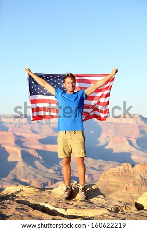 American USA flag - tourist in Grand Canyon. Happy young man hiking and cheering at Grand Canyon south rim during summer holidays in the United States. Young male hiker in his 20s.