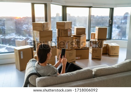 Home move out of apartment moving boxes woman using online movers services on mobile phone app easy pick-up with packages for new home. Asian new homeowner girl happy sitting in sofa. Photo stock © 
