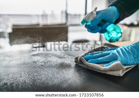 Sanitizing surfaces cleaning home kitchen table with disinfectant spray bottle washing surface with towel and gloves. COVID-19 prevention sanitizing inside.
