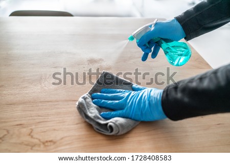 Surface cleaning spraying antibacterial sanitizing liquid with bottle washing table top at home . Man using gloves and towel doing spring cleaning.
