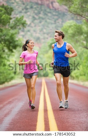 Two people jogging for fitness running on road outside in beautiful landscape nature. Woman and man sports athletes training for marathon. Couple together, Asian woman, Caucasian man,