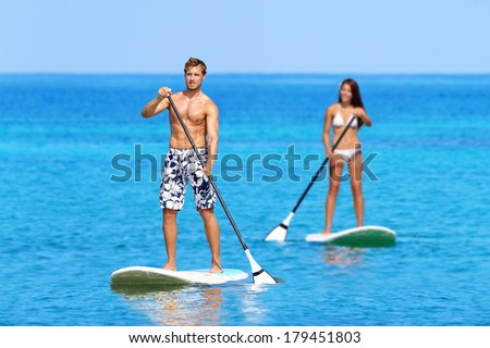 Paddleboard beach people on stand up paddle board surfboard surfing in ocean sea on Big Island, Hawaii Beautiful young multi-ethnic couple, mixed race Asian woman and Caucasian man doing water sport.