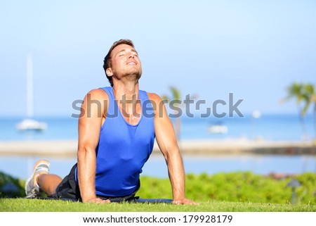 Fitness yoga man in cobra pose stretching abs stomach muscles. Fit male sports model doing stretching exercise outdoor in summer on grass. Handsome young male sports instructor.