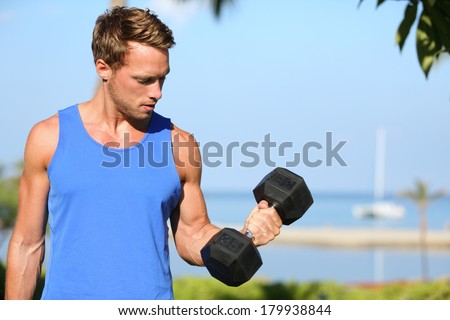Bicep curl - weight training fitness man outside working out arms lifting dumbbells doing biceps curls. Male sports model exercising outdoors as part of healthy lifestyle.