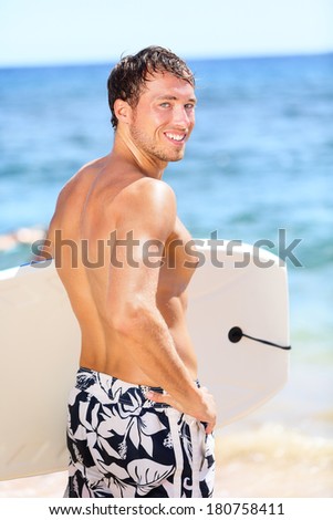 Handsome male surfer portrait on summer beach. Bodyboarding surfing man good looking standing with bodyboard surfboard during vacation holidays getaway. Caucasian water sport model in his 20s.