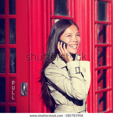London woman on smart phone by red phone booth. Young casual female business woman having conversation on mobile smart phone in London, England, United Kingdom. Multiracial Asian Caucasian model