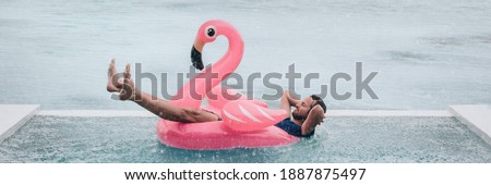 Happy man relaxing in swimming pool flamingo float despite bad rain weather. Travel summer vacation banner