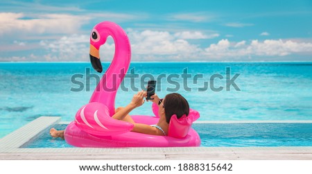 Relaxing woman floating in flamingo inflatable swimming pool toy at luxury resort using mobile phone sunbathing. Caribbean travel vacation hotel lifestyle.
