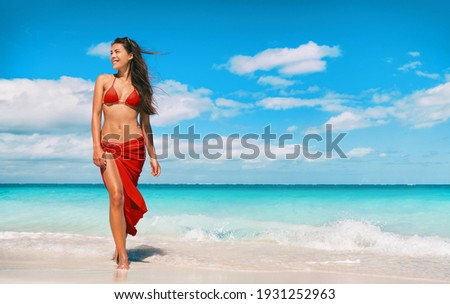 Beach bikini model in red swimsuit and skirt for wellness spa luxury. Hair removal laser treatment for legs and body summer ready vacation Asian woman walking relaxing at Caribbean travel holiday.