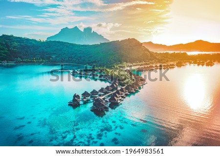 Luxury travel vacation aerial of overwater bungalows resort in coral reef lagoon ocean by beach. View from above at sunset of paradise getaway Bora Bora, French Polynesia, Tahiti, South Pacific Ocean