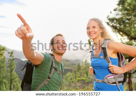 People hiking - couple on hike in forest. Hikers talking and pointing enjoying trek in beautiful mountain forest landscape. Blonde woman hiker and Caucasian man, Gran Canaria, Canary Islands, Spain.