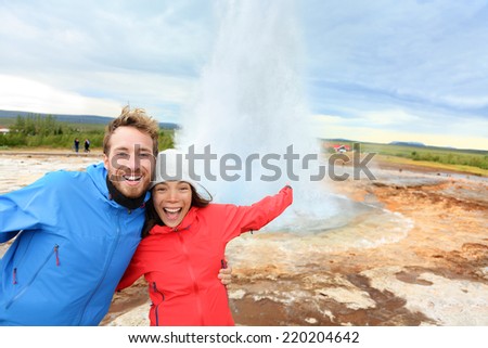 Iceland tourists fun by Strokkur geyser happy visiting famous tourist attractions and landmarks on the Golden Circle. Happy multiracial travel couple on holiday vacation sightseeing Icelandic nature.