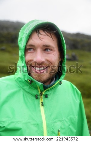 Rain jacket - man smiling outdoors on rainy day. Portrait of male model wearing green rain jackets outside living outdoor lifestyle.