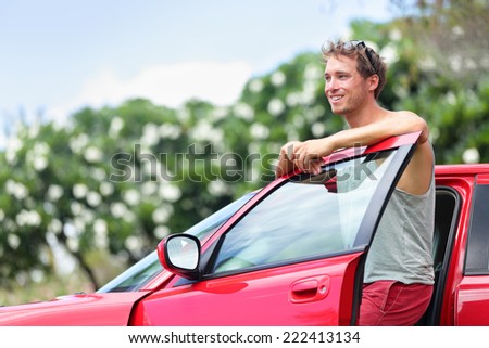 Car owner - young man and new red car outside. Happy male model leaning on door of a red sports car smiling.