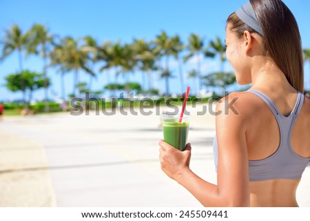 Woman drinking vegetable Green detox smoothie after fitness running workout on summer day. Fitness and healthy lifestyle concept with beautiful fit mixed race Asian Caucasian model outside on beach.