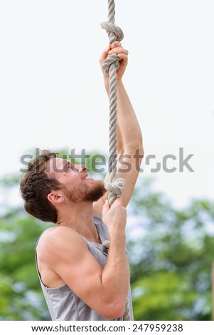Crossfit man doing rope climb workout outside during summer. Handsome male athlete climbing up rope for strength training session.