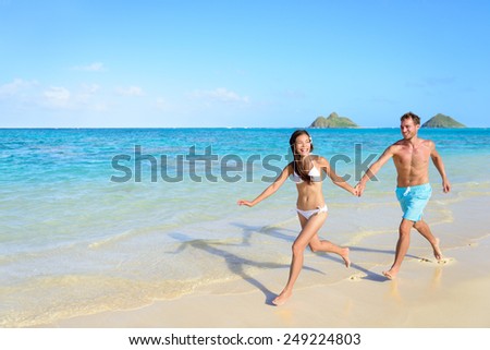 Beach vacations - happy couple running together joyful in water during holidays in Hawaii.