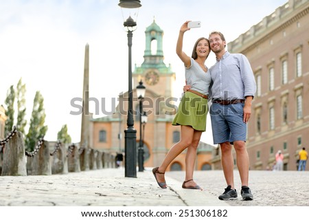 Selfie couple taking pictures at Stockholm cathedral and royal palace in Gamla Stan (Old Town) in the capital of Sweden. Tourists people taking travel photos with smartphone on summer holidays.