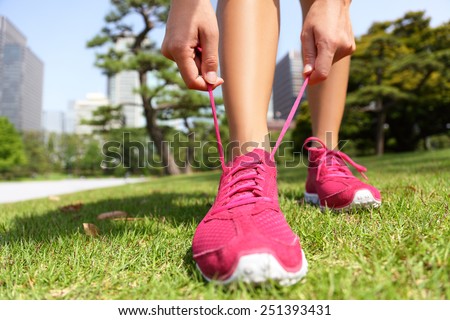 Runner getting ready for jogging tying running shoes laces - Woman preparing before run putting on trainers in japanese park near Ginza in Tokyo, Japan
