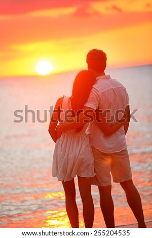 Honeymoon couple romantic in love at beach sunset. Newlywed happy young couple hugging enjoying ocean sunset during travel holidays vacation getaway. Interracial couple, Asian woman, Caucasian man.