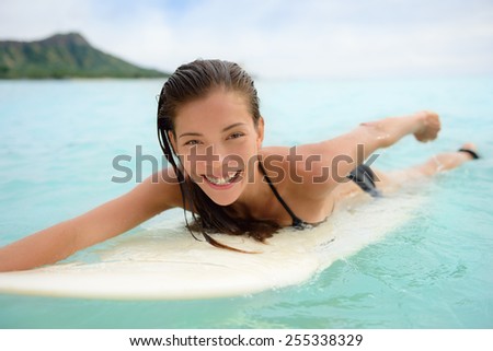Portrait of surfer woman surfing having fun on Waikiki Beach, Oahu, Hawaii. Female bikini girl laughing on surfboard smiling happy living healthy lifestyle on Hawaiian beach. Asian Caucasian model.