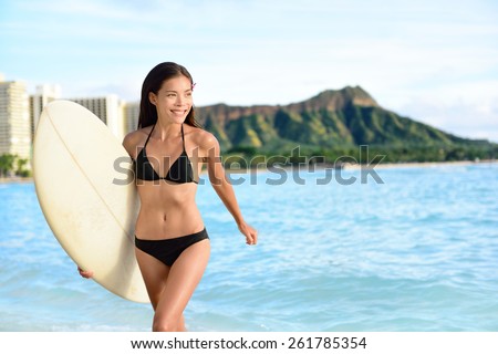 Portrait of surfer woman on Waikiki Beach, Oahu, Hawaii. Female attractive bikini girl running with surfboard happy having fun living healthy active lifestyle on Hawaiian beach. Asian Caucasian model.