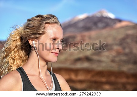 Running girl with earphones - woman runner listening to music in earbuds. Female athlete portrait after running in beautiful nature. Healthy lifestyle concept with beautiful young blonde fitness model