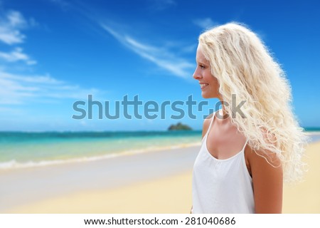 Blonde woman with long curly natural blond hair on beach in tropical paradise. Female model in her 20s smiling happy in profile.