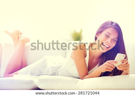 Smartphone woman using app on mobile cell phone smiling happy. Beautiful multicultural young woman model using smart phone texting sending text message lying on sofa. Mixed race Asian Caucasian girl.