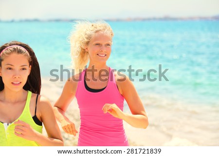 women running fitness jogging. Two pretty female fit friends training exercising fitness. Smiling Caucasian woman and focused multiracial Asian woman during workout in sunshine.