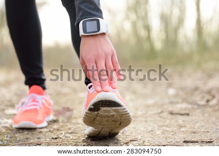 Runner stretching leg before run. Closeup of running shoes of a female jogger touching toe wearing a wearable tech - sportswatch activity tracker or smartwatch used as a heart rate monitor for cardio.