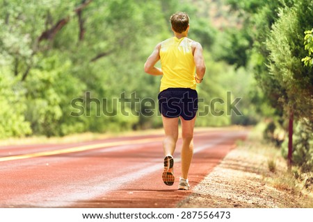 Running man runner working out for fitness. Male athlete on jogging run wearing sports running shoes and shorts working out for marathon. Full body length view showing back running away.