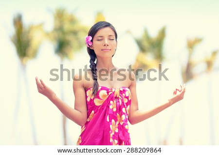 Serene meditation. Woman meditating on Hawaiian palm beach in sarong, hands up. Beautiful biracial female model enjoying sun in worship and meditation zen. Big Island, Hawaii, USA.