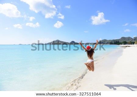 Christmas beach travel vacation woman in Santa hat jumping of joy on tropical Caribbean winter holidays getaway. Beautiful girl in bikini having fun under the sun traveling.