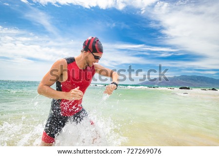 Smartwatch triathlon swimming sport man finishing swim checking heart rate on smart watch. Male triathlete swimmer running out of ocean. Professional athlete in triathlon suit training for ironman. Imagine de stoc © 