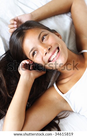 Beautiful young ethnic mixed race asian / caucasian woman talking on the phone while lying in the bed.