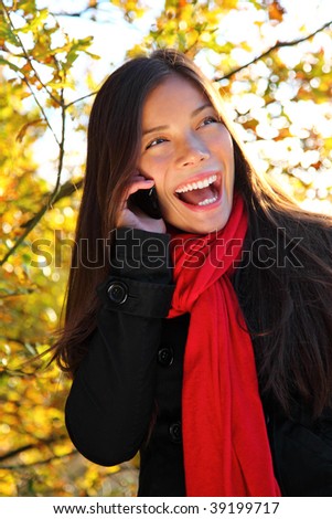 Happy laughing young woman on cell phone outside in park. Beautiful mixed race caucasian / asian woman,