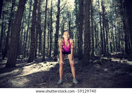 Woman running in forest. Female runner taking a break from running in beautiful forest with lots of mood / atmosphere and copy space. Beautiful young female athlete.