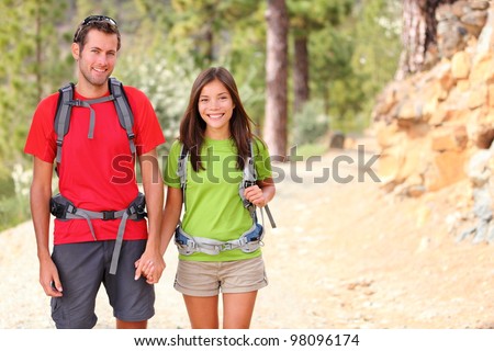 Hiking. Hiker couple portrait. Hikers walking in forest during camping travel hike. Healthy lifestyle photo of Asian woman and Caucasian man holding hands.
