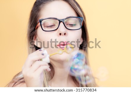 Beautiful young blond girl blowing soap bubbles, over yellow