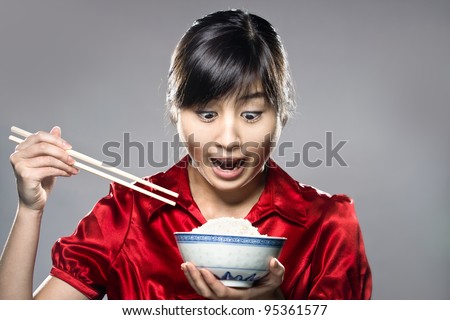 A young happy Asian girl eating rice with bowl and chopsticks