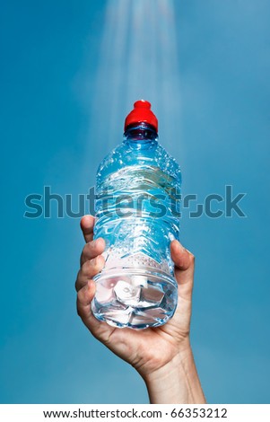 A bottle of water held against a blue sky in an authentic sunbeam
