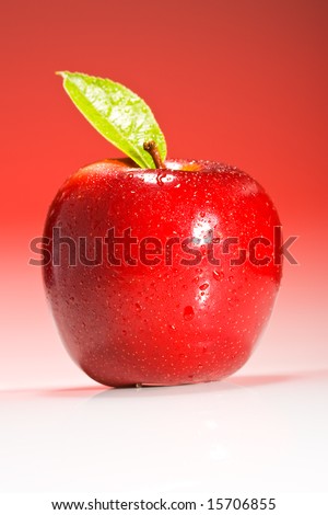 Shinny red apple on red gradient background with green leaf and water droplets