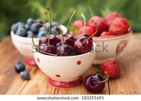 Summer berries in bowls on wooden table, fruits, cherry, raspberry, strawberry and blueberry