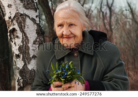 Spring portrait of the smiling elderly woman, in a forest with spring flowers