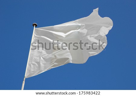 White flag flying in a stiff breeze against a clear blue sky.