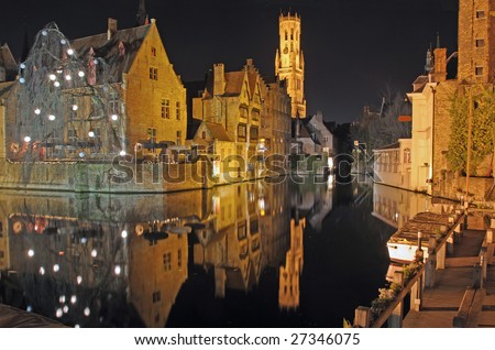 Night time scene of center town buildings and bell tower reflected in canal in Brugge, Belgium