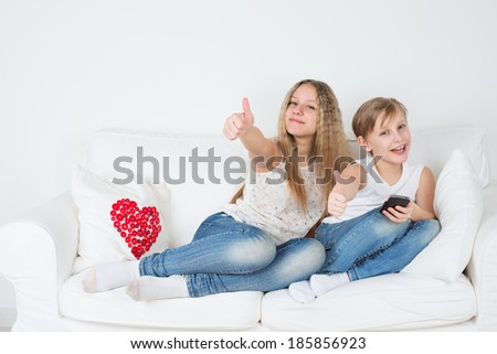 Boy and girl sitting on a couch and showing thumbs up