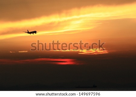 Silhouette of passenger jet airplane landing at sunset at Hong Kong International Airport.